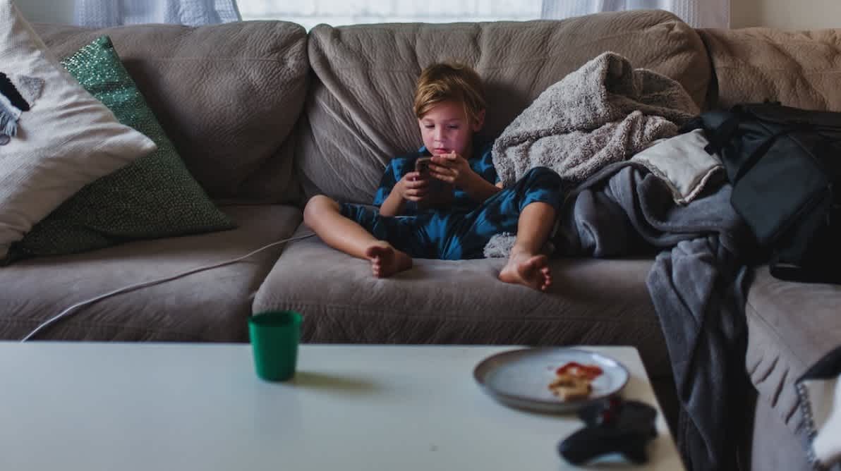 Gutt sitter i sofa og ser pĂ„ en telefon