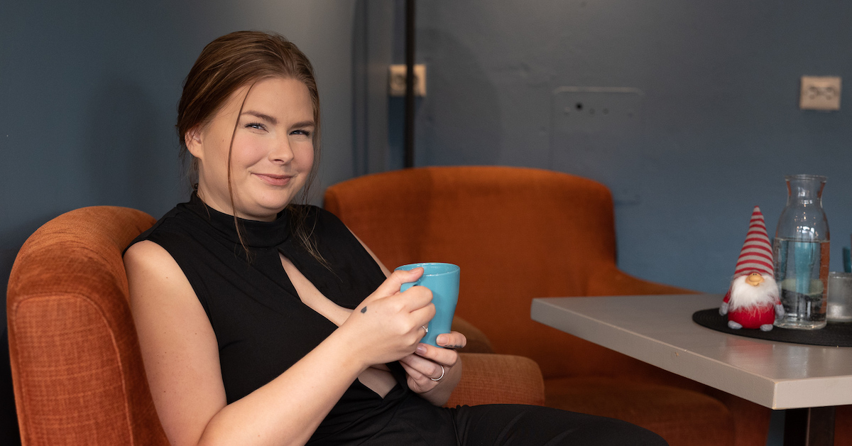 Smilende dame i en stol, holdende på en kaffekopp