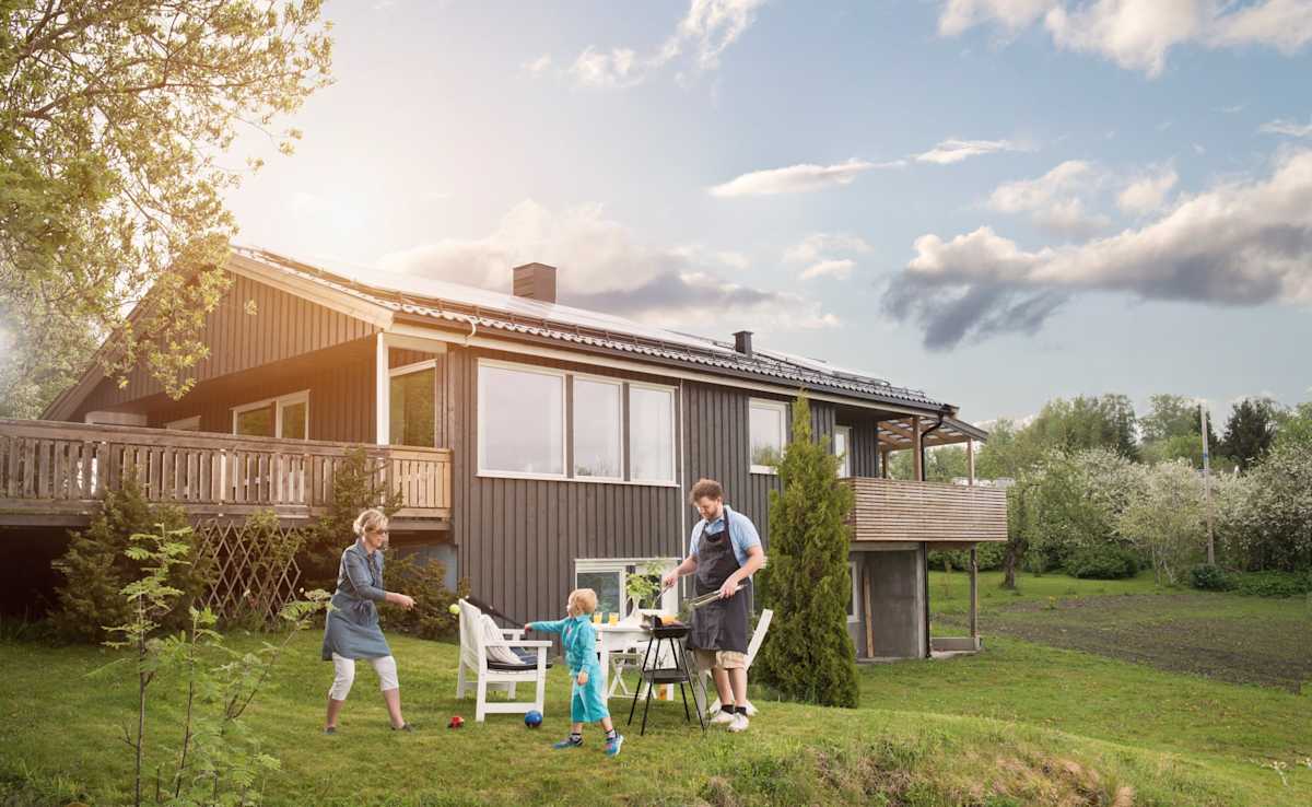 En familie griller og leker i hagen foran et hus med solcellepanel på taket