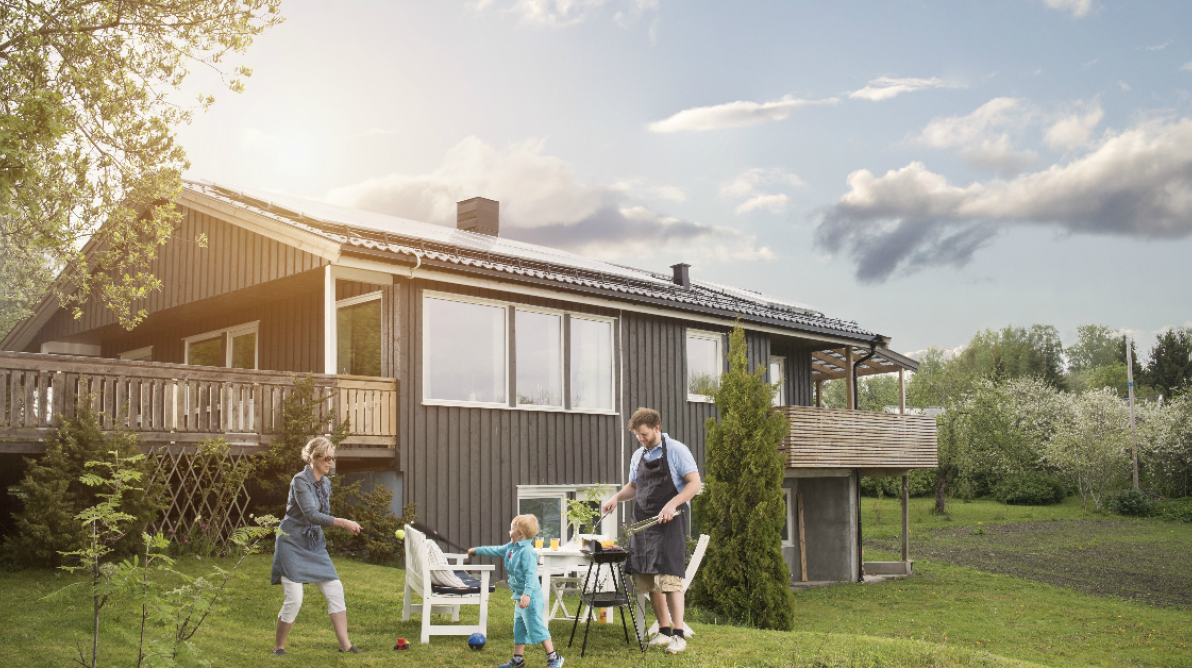 Familie griller og leker i hagen til et hus med solceller pÄ taket