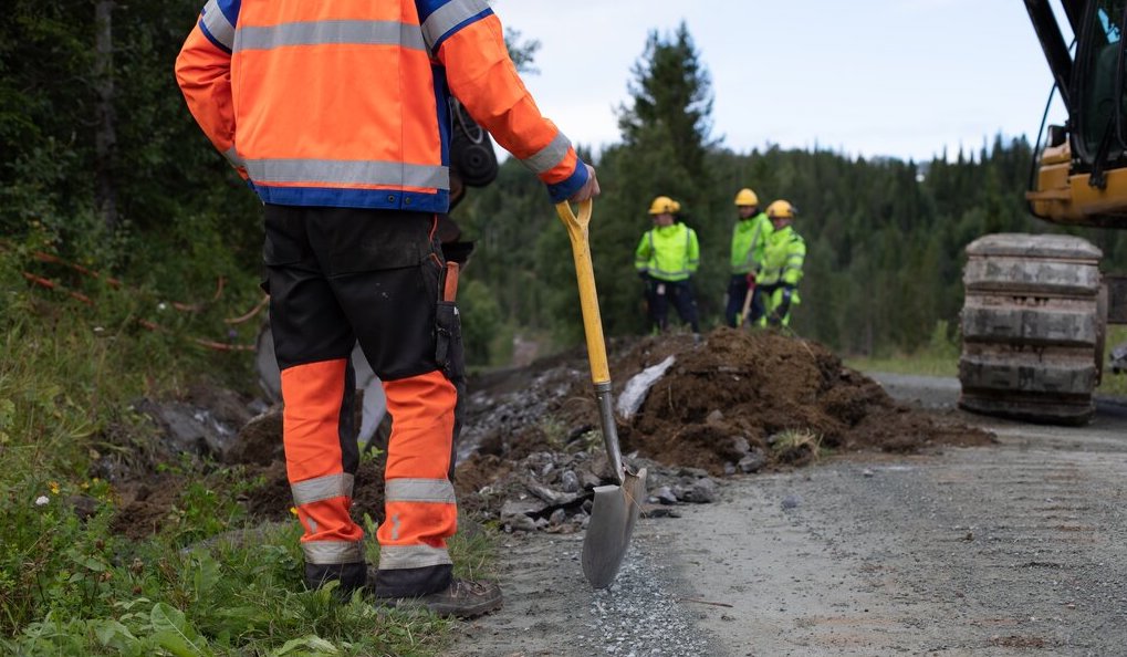 En mann lener seg på en spade, tre menn og en gravemaskin i bakgrunnen