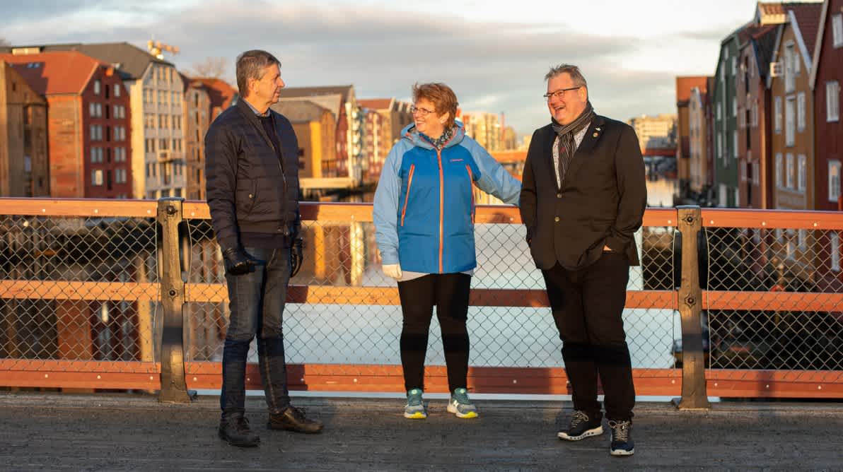 Bilde av tre smilende mennesker på en bro