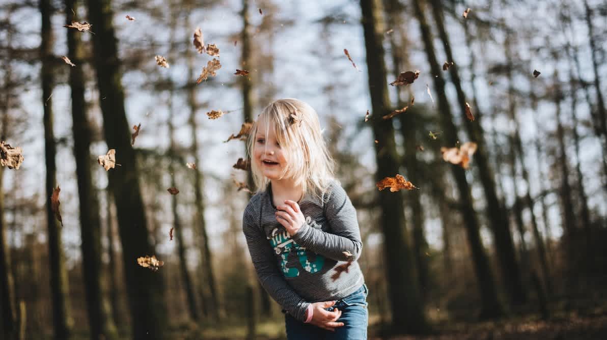 Liten jente ute i skogen bland fallende blad