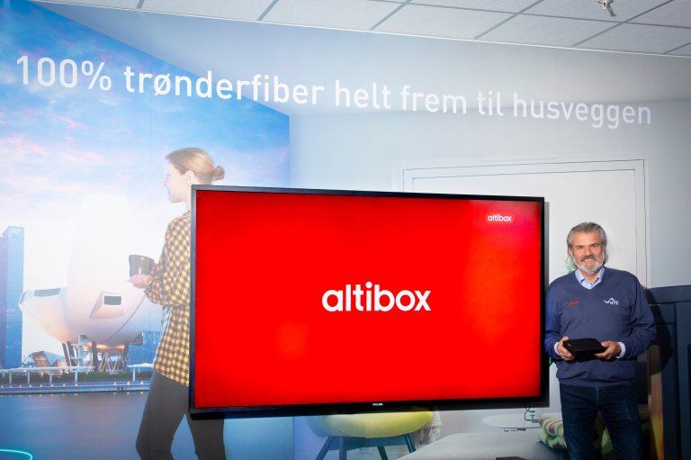 Mann stÄr forran en stor TV med Altibox logo pÄ skjermen
