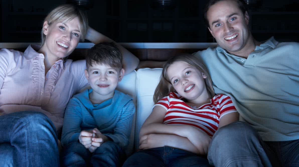 Familie sitter pÄ sofa forran en TV