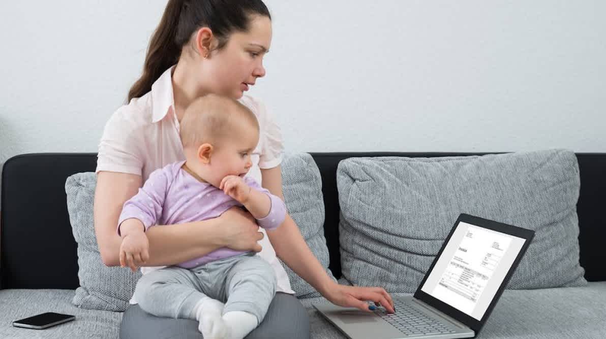 Dame med en baby pÄ fanget ser pÄ en faktura pÄ PC-skjermen