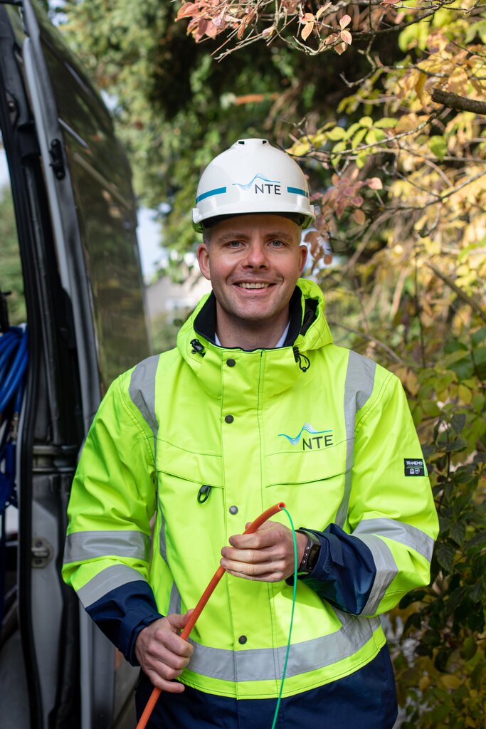 Mann i synlighetsklĂŠr og hjelm holder en fiberkabel i hendene