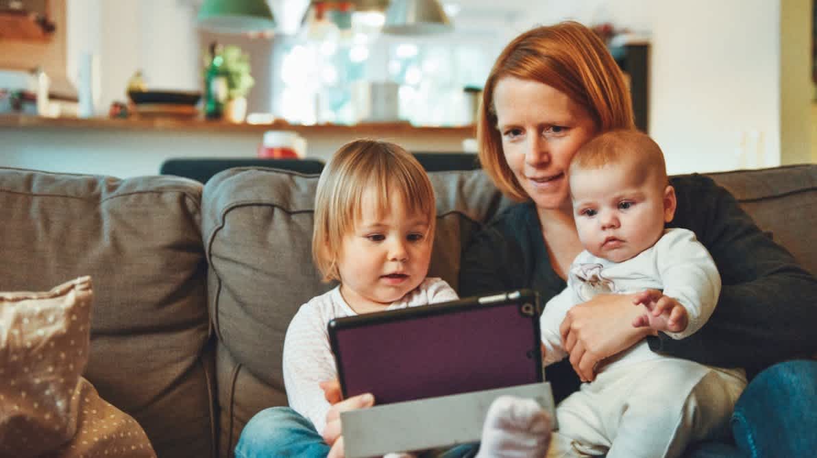 Mor og to barn sitter sammen og ser pÄ en iPad