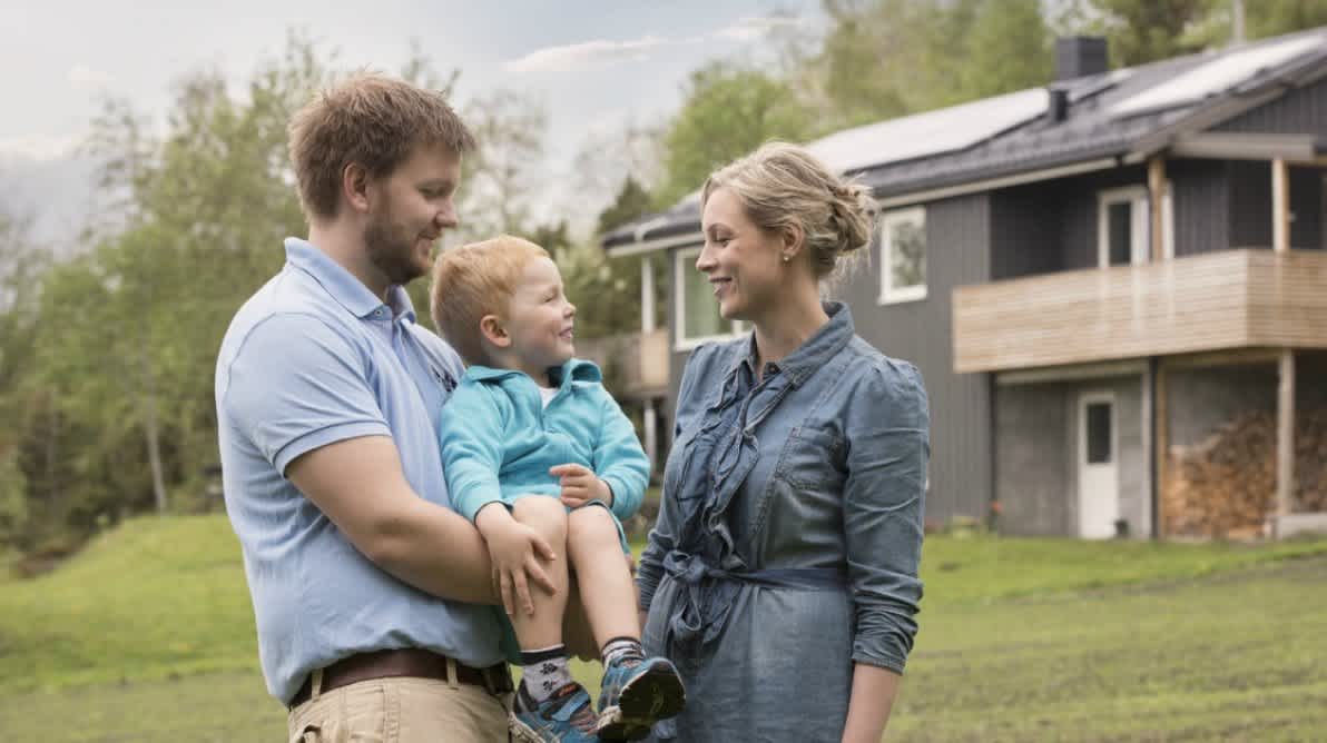Mann og dame holder en baby foran et hus
