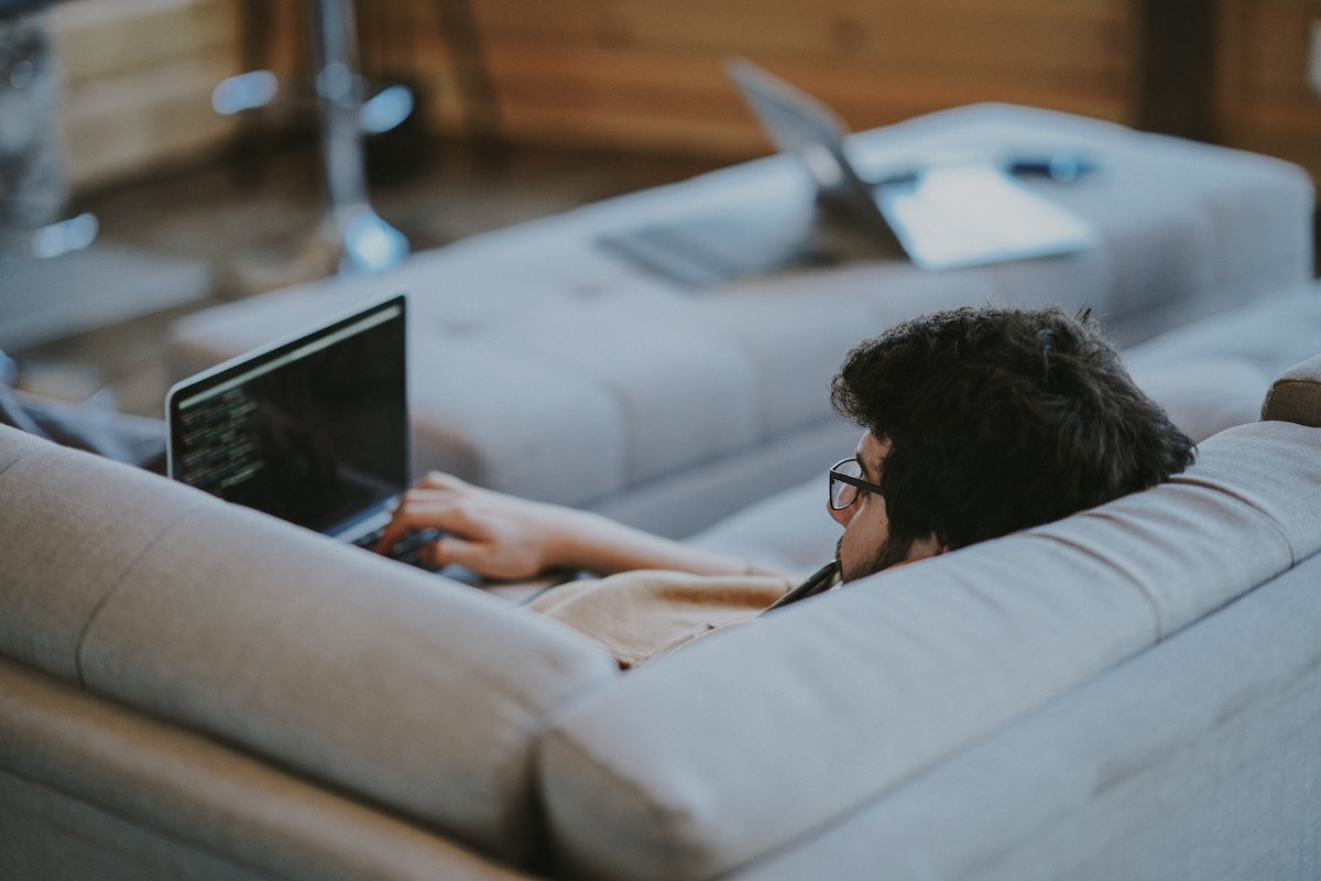 Mann ligger henslengt i sofaen med mac-en