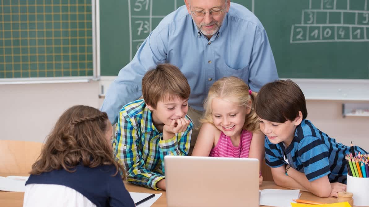 Barn på skolen ser på en laptop sammen med sin lærer