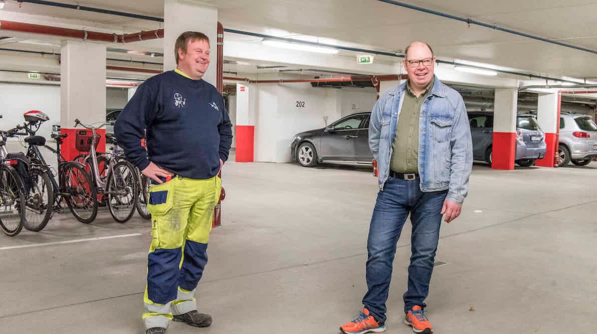En elektriker og en mann i dongeriklær smiler
