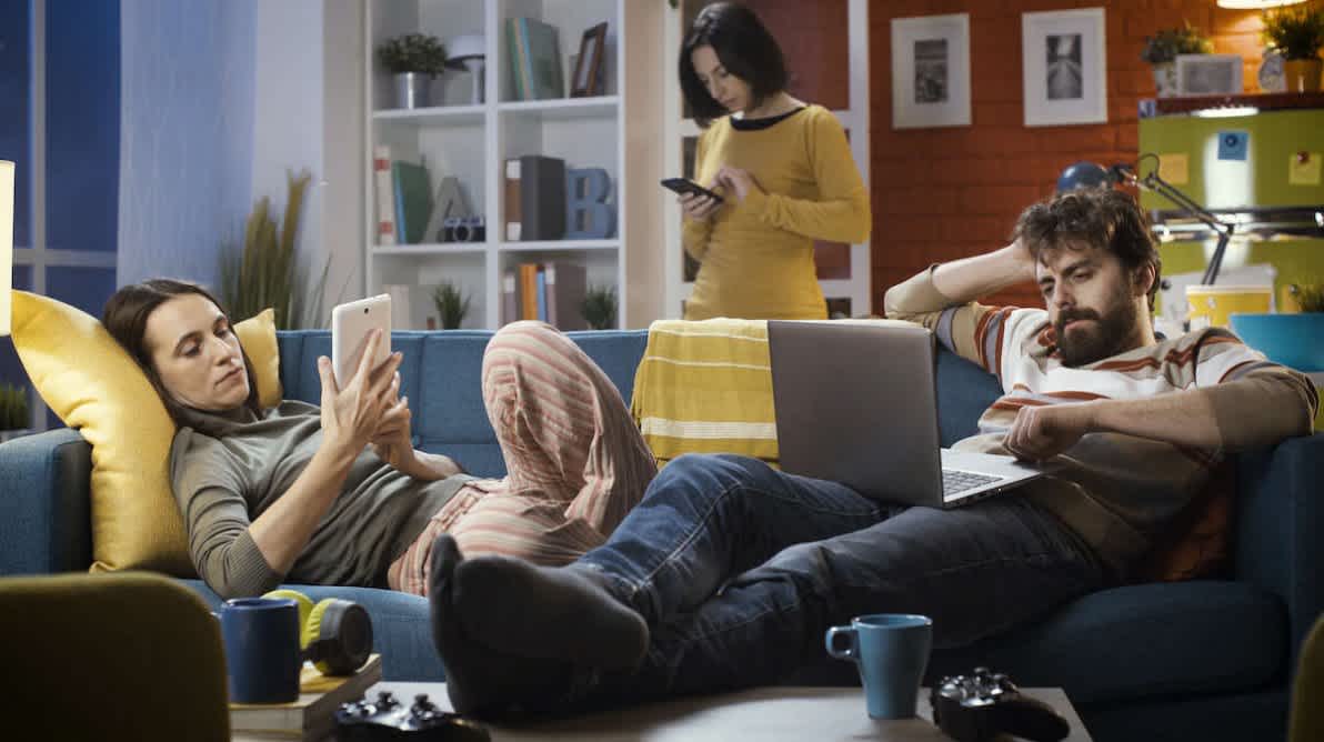 3 venner slapper av i stua med hver sin datamaskin og smarttelefon