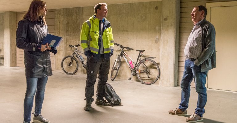 Bilde av tre personer som står sammen og snakker i en kjeller