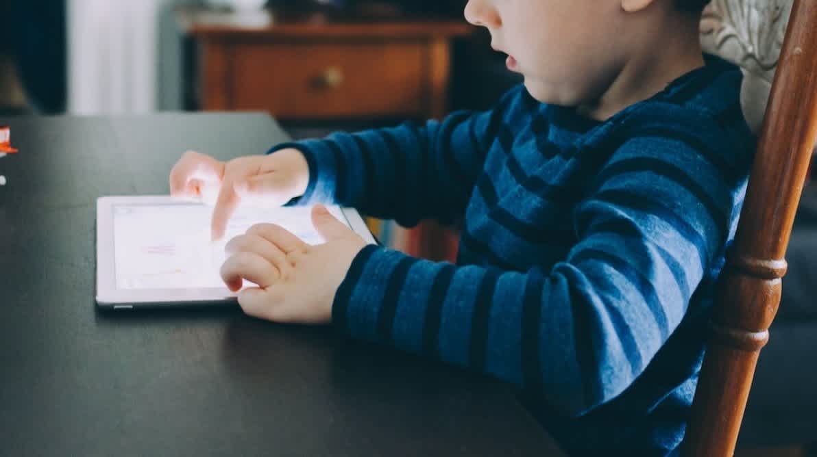 En gutt sitter foran et bord og trykker pÄ en iPad