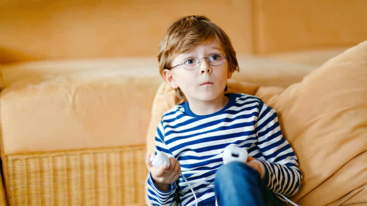 Gutt sitter på sofa og gamer på en TV utenfor bildet