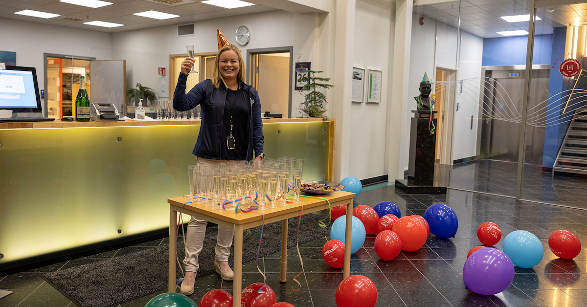Smilende dame med partyhatt som serverer brus og sjokolade omgitt av ballonger