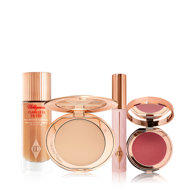 Flawless Pillow Talk Glow makeup kit displayed A makeup kit with a glowy primer in a glass bottle with a gold-coloured lid, a pressed powder compact with a mirrored-lid in a soft beige shade, mascara in a nude pink-coloured tube with a gold-coloured lid, and a lip and cheek tint compact with a mirrored-lid in a berry-rose shade.