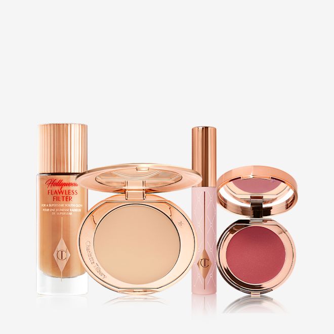 Flawless Pillow Talk Glow makeup kit displayed A makeup kit with a glowy primer in a glass bottle with a gold-coloured lid, a pressed powder compact with a mirrored-lid in a soft beige shade, mascara in a nude pink-coloured tube with a gold-coloured lid, and a lip and cheek tint compact with a mirrored-lid in a berry-rose shade.