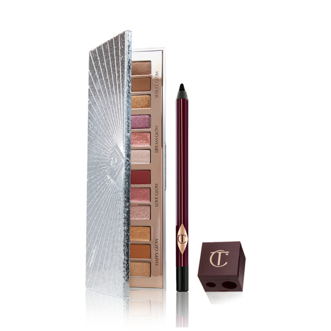 An open eyeshadow palette with twelve eyeshadows in matte and shimmery shades in pink, purple, red, gold, brown, and cream, an eyeliner pencil in black, and a lip and eye pencil sharpener. 