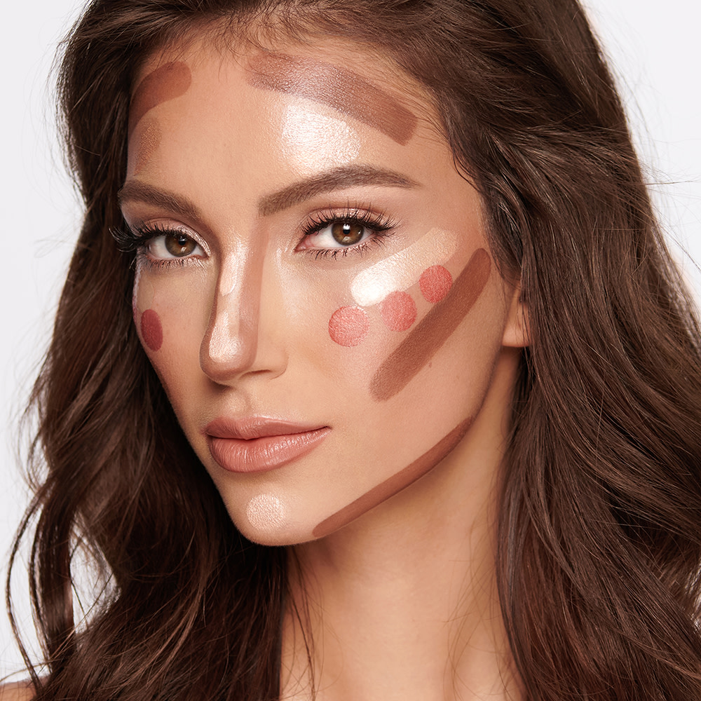 A medium-tone brunette model with blush, highlighter, and contour applied but not blended yet. 