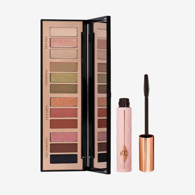 Smokey Eyes Are Forever Kit open Black mascara in a sheer pink tube with a gold coloured lid and fluffy applicator and an open, 12-pan eyeshadow palette with a mirrored-lid with pink, gold, green orange, red, brown, black, and beige shades to create different smokey eye looks.
