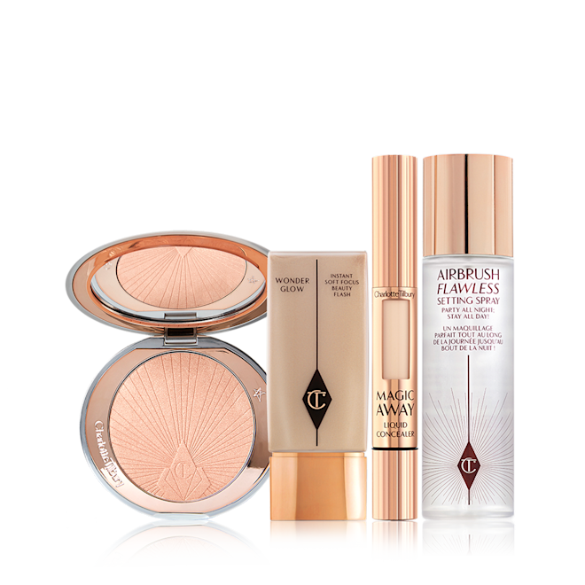 Charlotte's Flawless Gold Secrets kit displayed An open, mirrored-lid highlighter compact in a light rose gold shade with a glowy primer in a translucent bottle with a gold-coloured lid, liquid concealer in a gold tube, and setting spray in a clear bottle with a gold-coloured lid.
