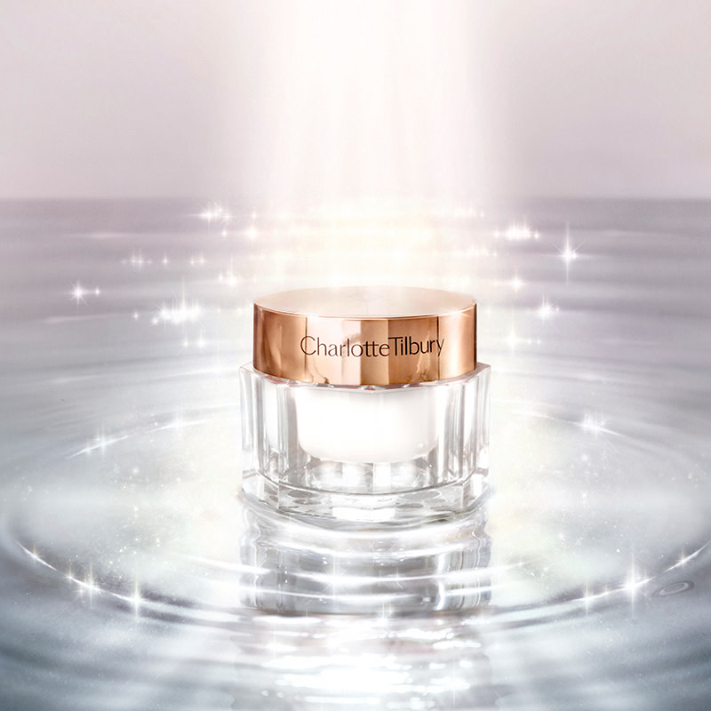 Pearly white face cream in a glass jar on top of glimmering water with light shining on it.