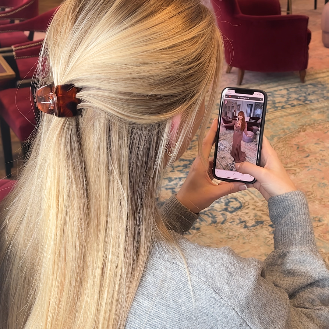 a blonde model holding up a phone that has a photo of Charlotte Tilbury wearing an evening gown displayed.