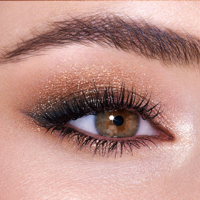 Single-eye close-up of a fair-tone model with hazel eyes wearing shimmery gold and brown eyeshadow. 