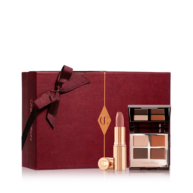 Iconic Secrets Mystery Box disaplayed A dark crimson-coloured gift box with an open lipstick in a nude pink shade with an open mirrored-lid quad eyeshadow palette with brown, red, and beige eyeshadows.