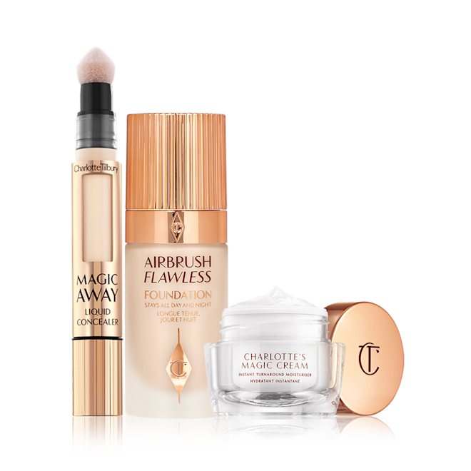 Charlotte's Magic Airbrush Complexion Kit displayed Creamy liquid concealer in a gold-coloured tube with a soft sponge applicator end, foundation in a frosted glass bottle with a gold-coloured lid, and pearly-white face cream in a glass jar with a gold coloured lid.