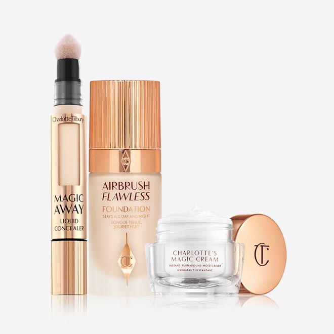 Charlotte's Magic Airbrush Complexion Kit displayed Creamy liquid concealer in a gold-coloured tube with a soft sponge applicator end, foundation in a frosted glass bottle with a gold-coloured lid, and pearly-white face cream in a glass jar with a gold coloured lid.