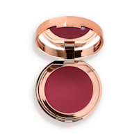 Pillow Talk Lip and Cheek Glow en Colour of Passion abierto Una polvera abierta con producto en crema para labios y mejillas, con tapa espejada, en un tono rojo baya.