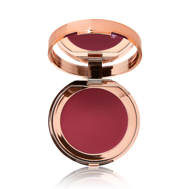 An open, mirrored-lid lip and cheek cream compact in a berry-red shade. 