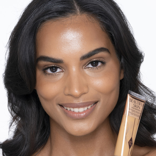 Dark-tone brunette model wearing glowy, skin-like foundation with a fresh, satin finish with a nude lipstick, and subtle eye makeup.