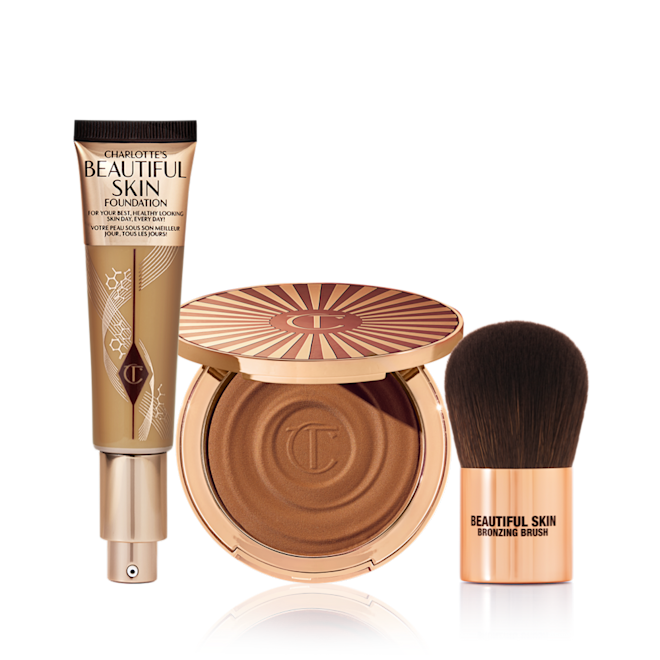 Sun-kissed Complexion Trio An open foundation tube with a pump dispenser, an open cream bronzer compact in gold packaging, and a bronzer brush with dark brown soft bristles and rose gold-coloured handle.
