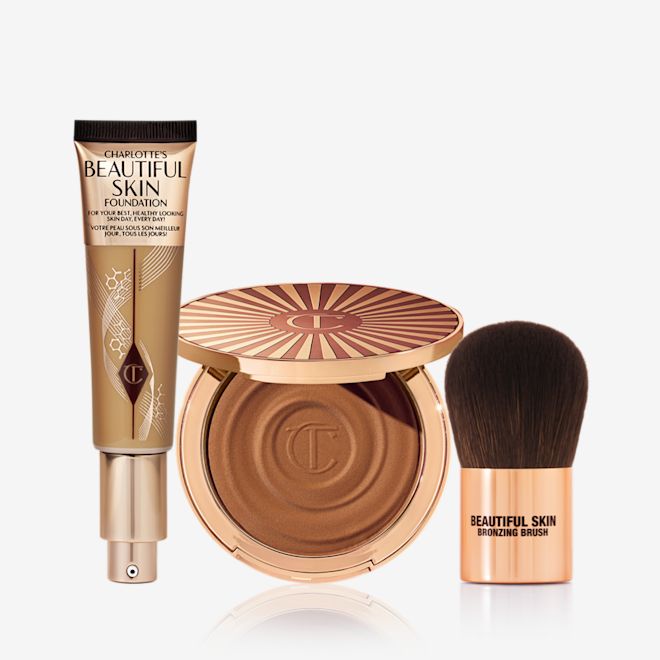 Sun-kissed Complexion Trio An open foundation tube with a pump dispenser, an open cream bronzer compact in gold packaging, and a bronzer brush with dark brown soft bristles and rose gold-coloured handle.