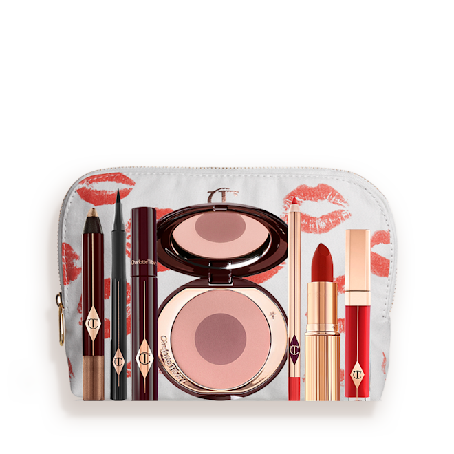 The Bombshell kit for fair to medium displayed A white makeup pouch with an open two-tone blush in cool-toned pink and brown with a mascara, eyeliner pen, chubby eyeshadow stick in gold, an open lipstick in bold red, lip liner pencil in blood-red, and a lip gloss in bright red.
