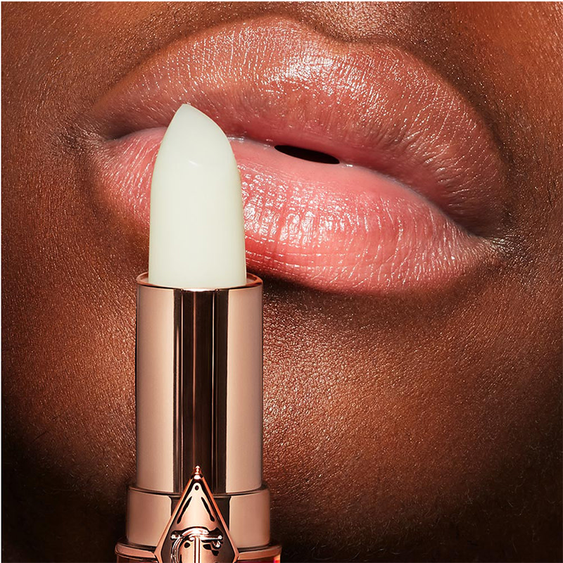 Close-up of a deep-tone model's plump and hydrated lips with a white-coloured lipstick conditioner in front of her lips. 