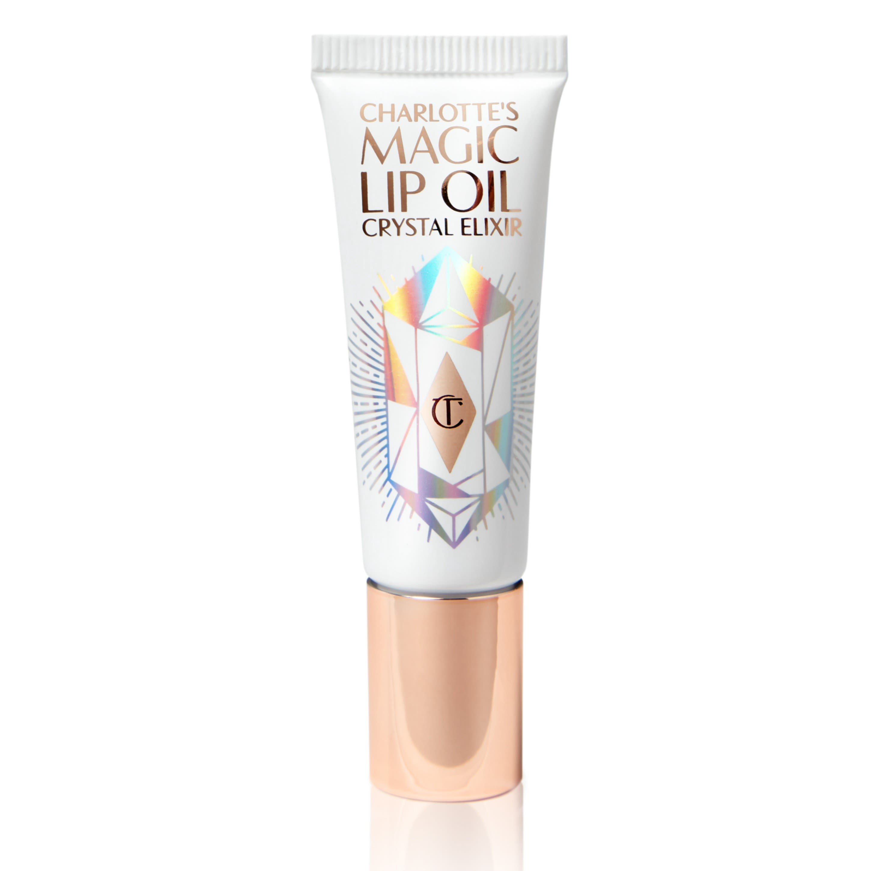 Magic Lip Oil Crystal Elixir closed A lip oil in a white coloured tube with reflective geometric patterns on it in silver colour and a rose-gold-coloured lid.
