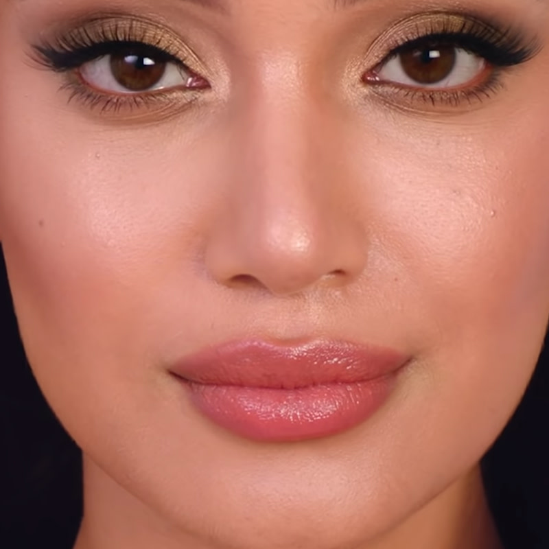 A light-tone model with brown eyes wearing smokey gold eyeshadow with volumising mascara, and nude pink lip gloss. 