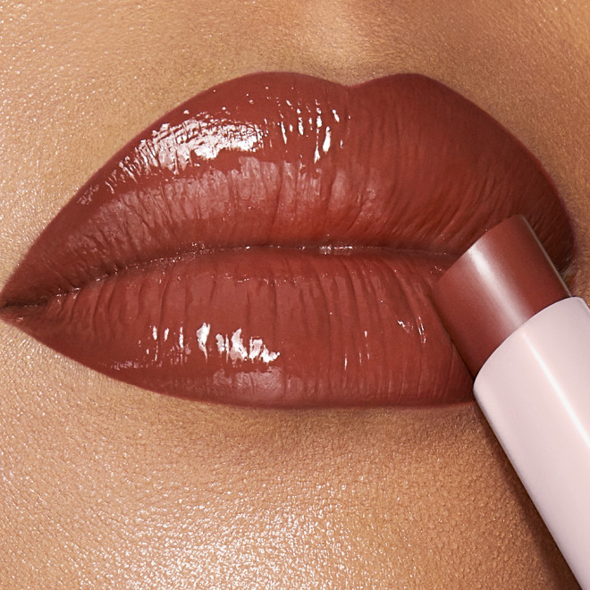 Lips close-up of a medium-tone model applying a moisturising lipstick balm in a soft brown shade.