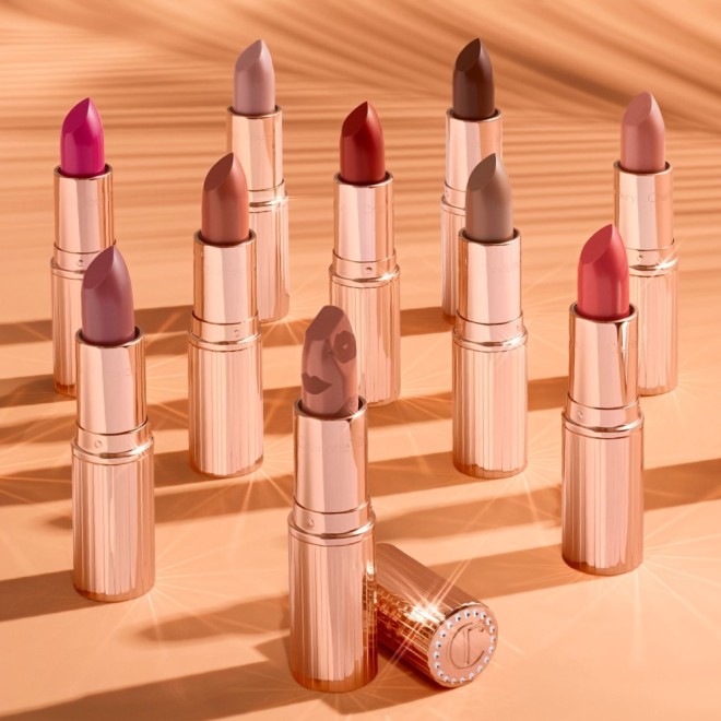 A collection of satin lipsticks in gold-coloured tubes in shades of peach, magenta, coral, brown, red, and nude pink. 