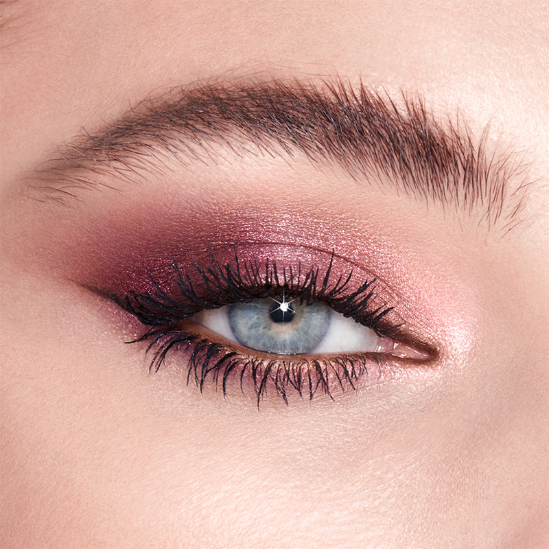 Single-eye close-up of a fair-tone model with blue eyes wearing shimmery rose gold and purple eyeshadow. 