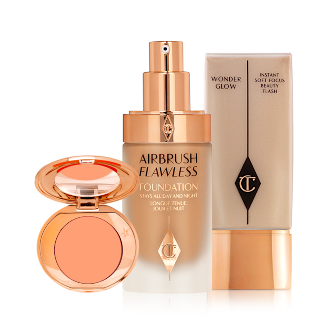 Magic Flawless Go Kit open An blush compact with a mirrored lid with a peach shade with an open foundation in a glass bottle with a gold pump dispenser and a glowy primer in a clear bottle with gold-coloured lid.