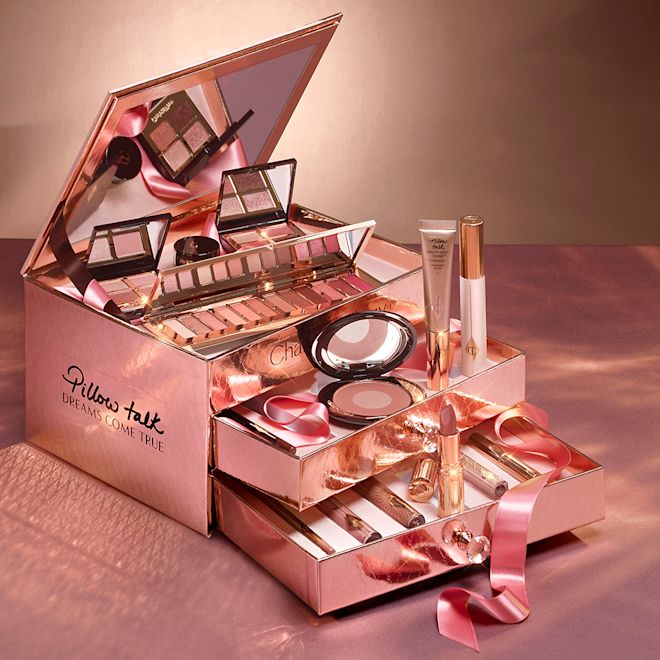 Pillow Talk Dreams Makeup Vault Box 2021 with the makeup products displayed A reflective, gold-coloured chest with two, opened drawers containing makeup items, which include Liquid highlighter wand in rose gold, black mascara, shimmery lip gloss in nude pink, glitter-free but high-shine lip gloss in nude pink, rose gold eyeshadow pigment in a petite pot, two closed lipsticks, travel-size lip gloss in nude pink, eyeliner pencil in dark brown, lip liner pencil in nude pink, quad eyeshadow palettes, 12-pan eyeshadow palette, and two-tone blush compacts.