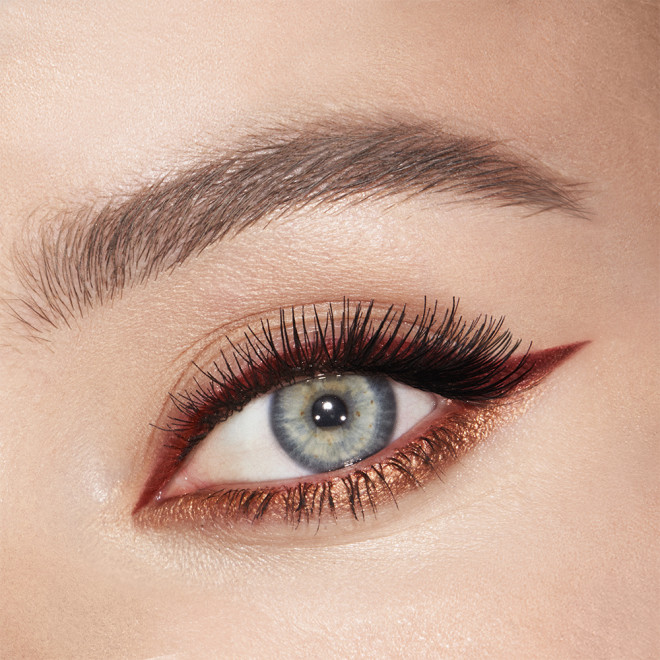 Eye close-up of a fair-tone, blue-eyed model wearing a matte, rust-coloured eyeliner on the upper lid and shimmery copper-coloured liner on the lower waterline. 