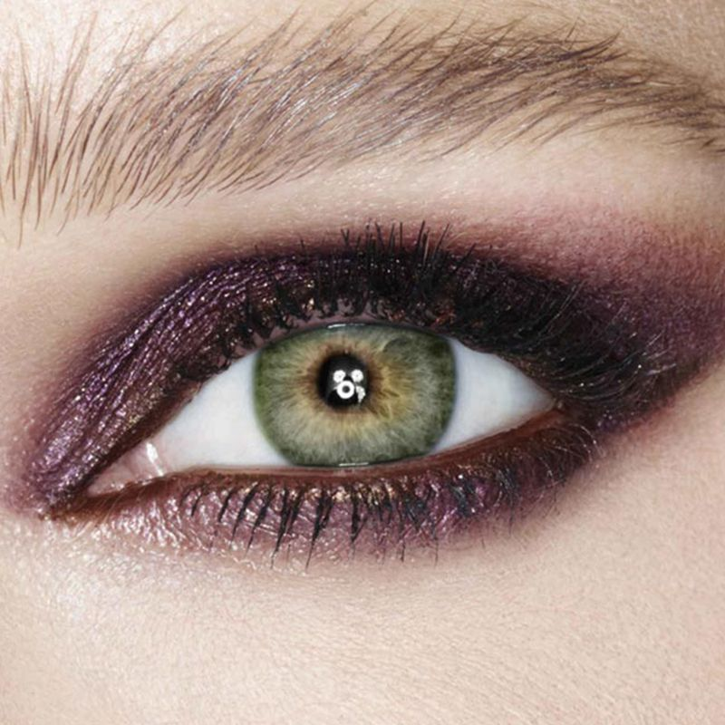 Eye close-up of a model with green eyes wearing shimmery, smokey purple eye makeup. 