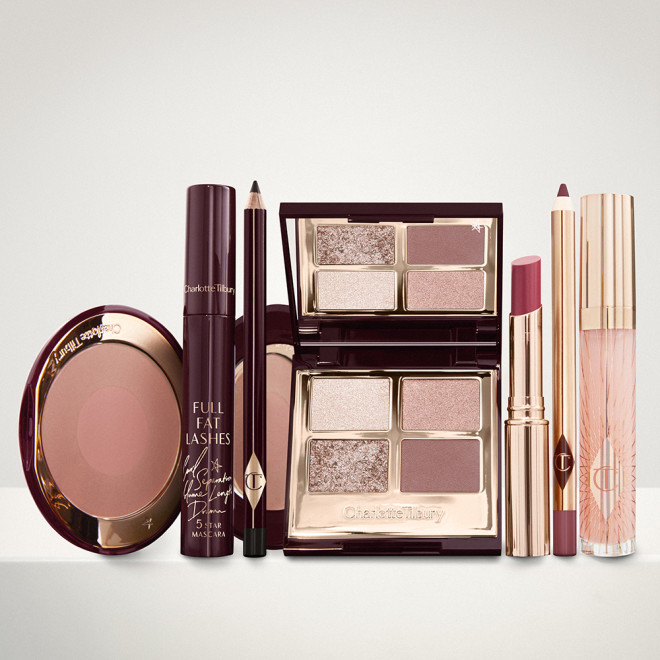 An open two-tone blush in cool-toned brown and warm pink with a mascara, eyeliner pencil, quad eyeshadow palette with shimmery and matte brown and golden shades, an open lipstick in nude red, lip liner pencil in maroon and a lip gloss in nude pink. 